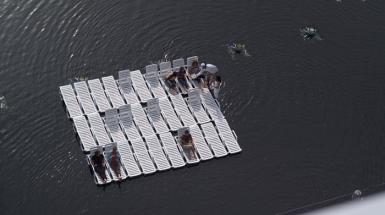 People sitting on raft made of white pool chairs. 