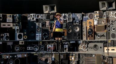 A performer is singing in the middle of a stage made of many stacked speakers