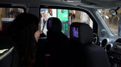A young woman looking closely at a screen in the back of a car seat headrest