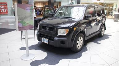3/4 front view of a black cube-like vehicle parked over top of a black fabric cut to look like an oil spill