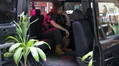 A young person sitting in the backseat of a vehicle contemplating a video in the headrest in front of them.