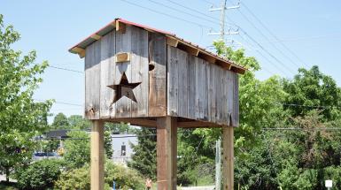 A large wooden shed with a star-shaped hole in the front, put up on stilts with an open bottom.