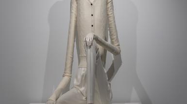Human sculpture with white skin, white clothes and hair, extremely long limbs and torso