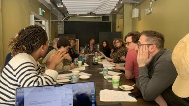 group of people sitting at a long desk with papers on the table, in discussion