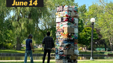 Image of a tower made from bales of compacted garbage. Two people stand in the park looking at it.