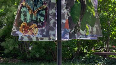 A black pole holds five banners depicting ink drawings of imagined characters. The banners billow outward in the wind.