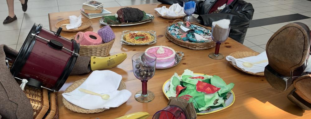 anthropomorphized thrifted objects that look like people sitting around a table with hand-crafted fake food 