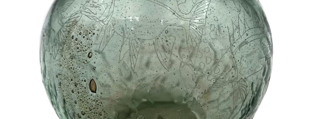 a circular glass vase etches with fish and other botanicals with a green hue