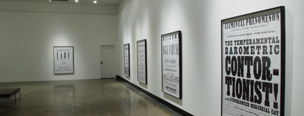 Image of gallery with multiple text based works hanging on walls. 