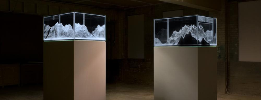 Image of two plinths with glass cases on top which hold models of mountains.