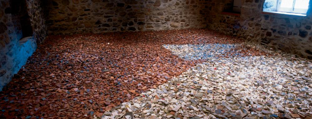 A brick room filled with broken tiles on the floor. There are two colours of tile white and red that are laid out in a geometric pattern.