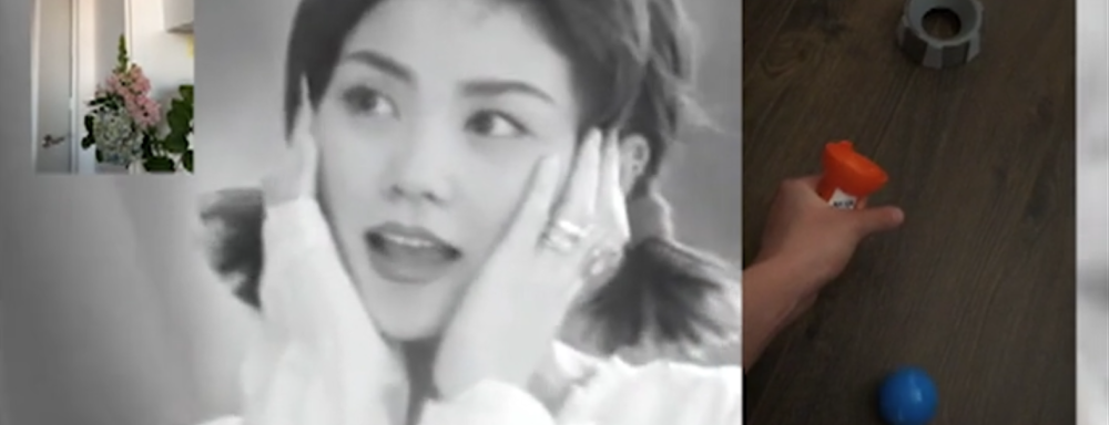 Screen shot of Video. Black and white image of woman in the Bckground holding her face. Image in foreground on left shows a plant in a room. Image in foreground on right shows hand playing with toy.