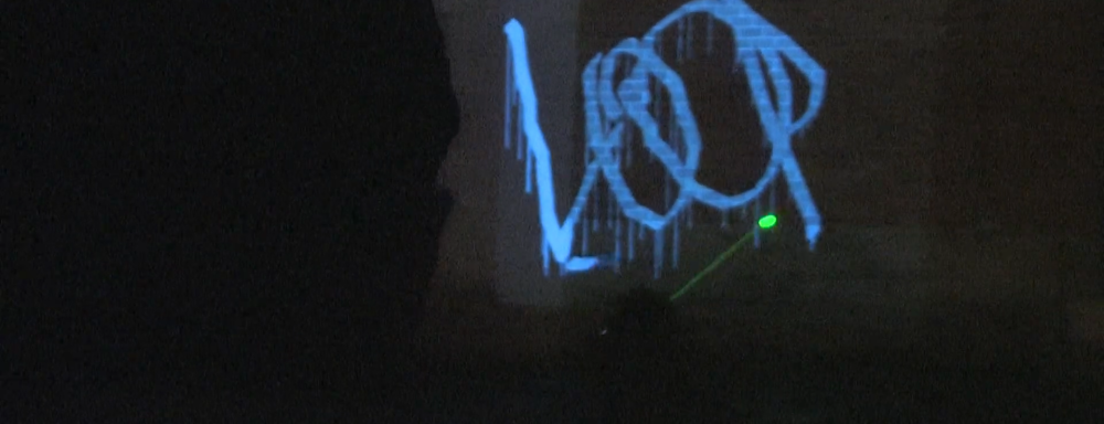 man using laser to draw projected graffiti that says "loop"