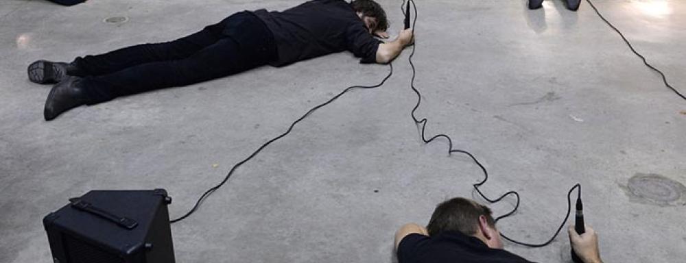 multiple men lying on the floor holding microphones which are pointing at the floor. 