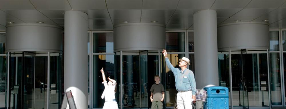 Three figures, an old man and young girl point to the sky. Young boy stands behind them.