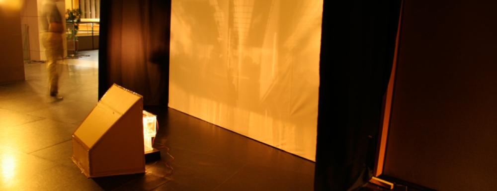 A projector in a cardboard structure shinning through a translucent box on to a screen. 