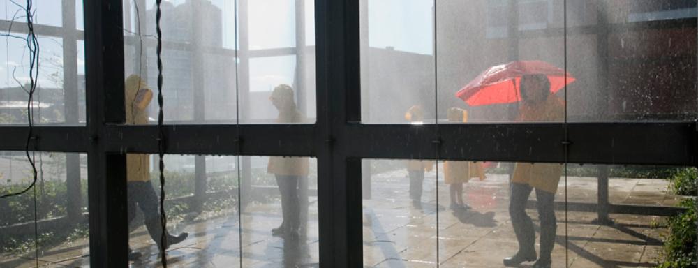 A view through a window to figures walking through mist in yellow rain jackets.