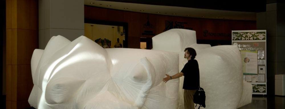 A man standing in front of two white abstractly shaped large blowup sculptures.