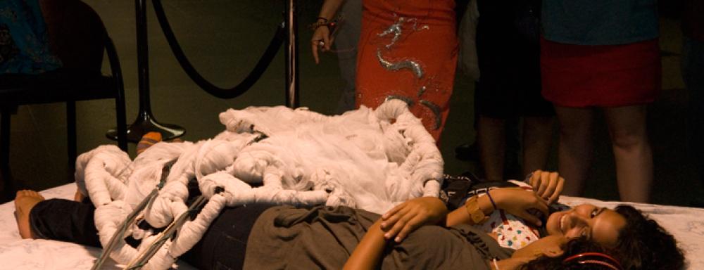 Two woman lying on bed with blanket that has wires coming from it. 