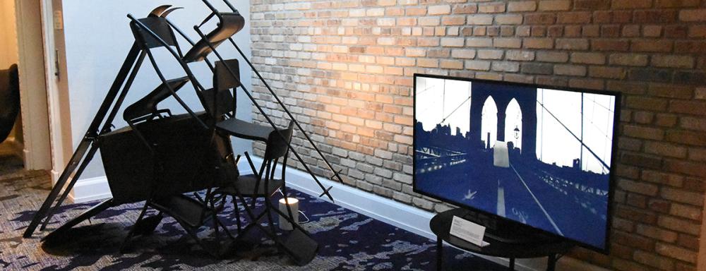 On the left chairs staked to for a tent like structure. On the right a Tv which is playing a video of a bridge.