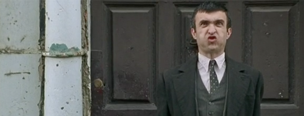 Still from John Duffy's Brother. Man with face of frustration who looks to be blowing air with hands at his side in fists. 