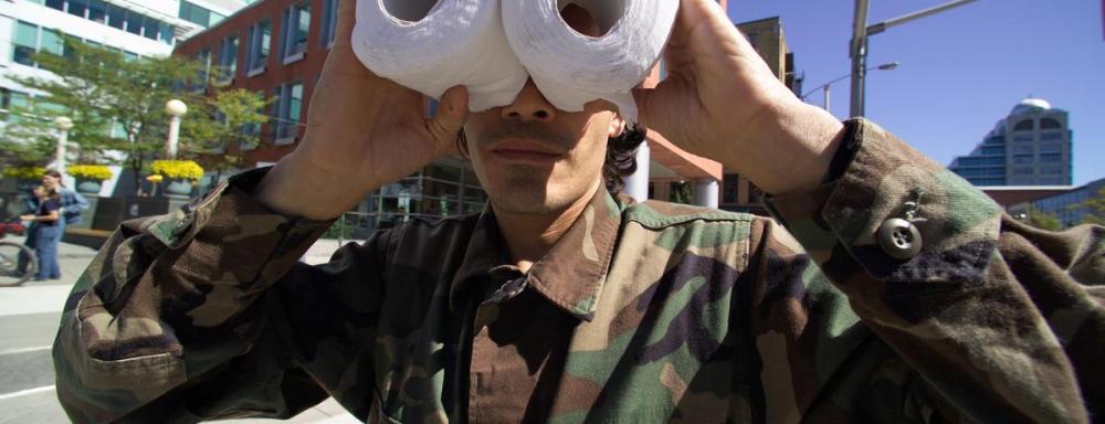 Person in military attire looking through two toilet paper rolls like binoculars 