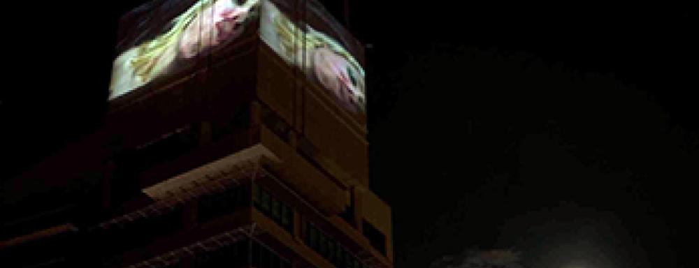 Large screens on top of building playing video of woman kissing camera