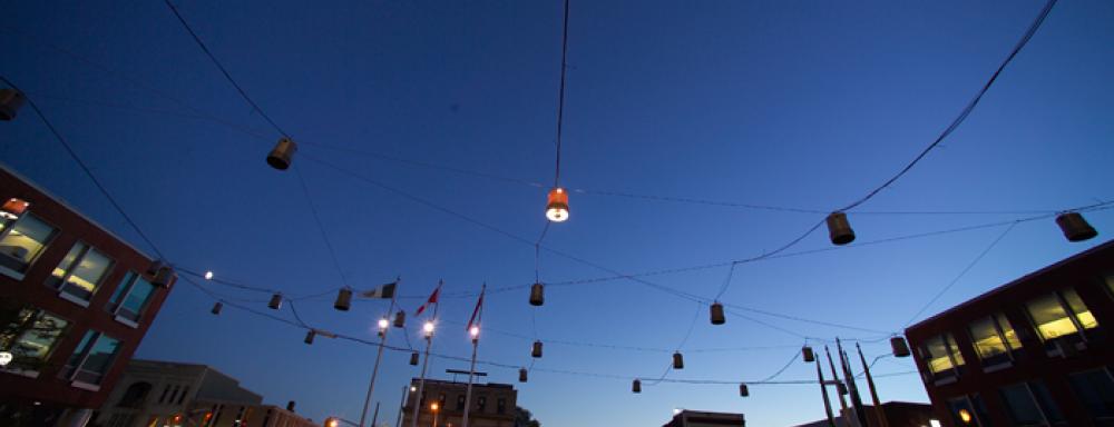 Street with strings and spotlights hanging above. Only one light is on