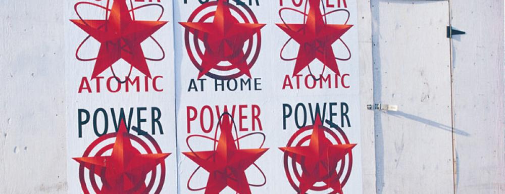 a series of ads that mix communist iconography and images of hydro electricity. 6 posters on wall each say power on top. 3 say at home on the bottom. 3 say atomic at the bottom. With red stars in the center. 