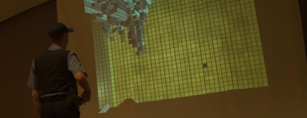 Visitor looking at projection of yellow grid with the top left corner a birds eye view of a city scape.