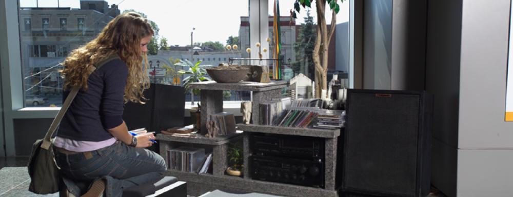 A woman crouching beside a radio shelving unit made of granite. 