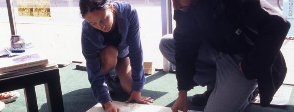 two people crouched pointing at map on floor