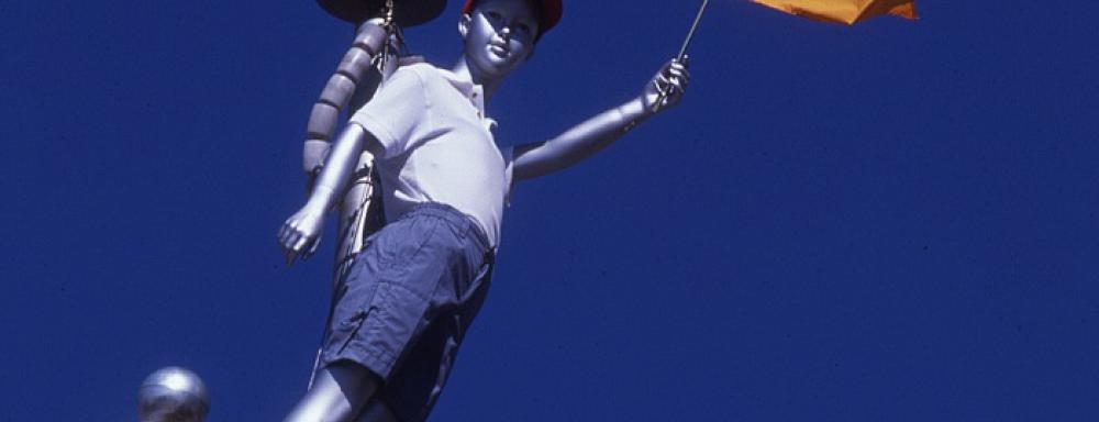 Sculpture of boy holding yellow flag atop a flag pole