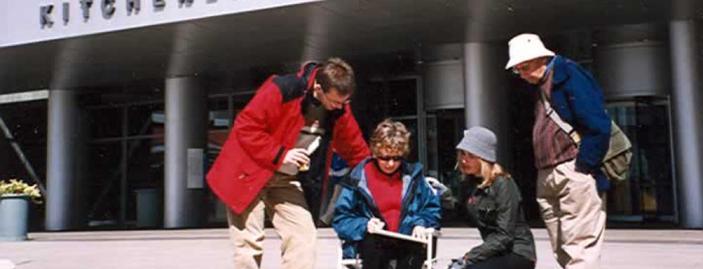 Three people looking over a figure sitting in chair drawing