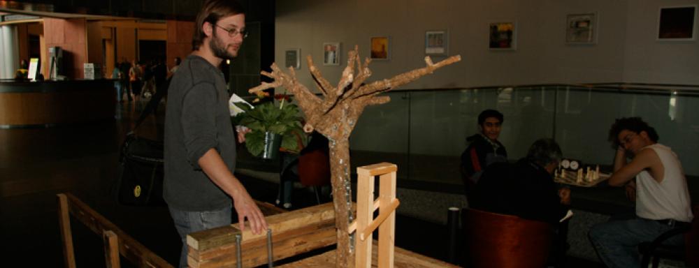 Man interacting with sculpture which features a small leafless tree
