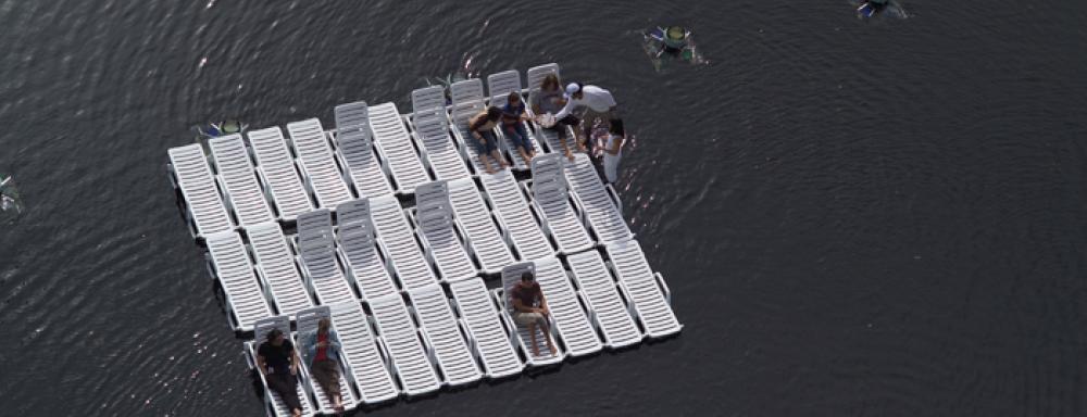 People sitting on raft made of white pool chairs. 