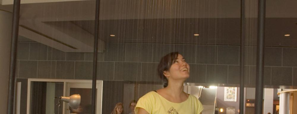 Woman standing in rain room with hands out. 