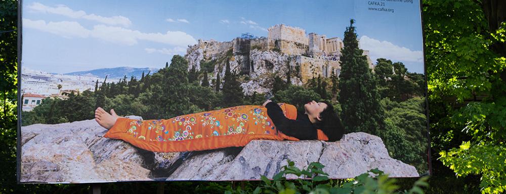 A billboard depicting the artist laying on the ground in the mountains under a silk blanket.