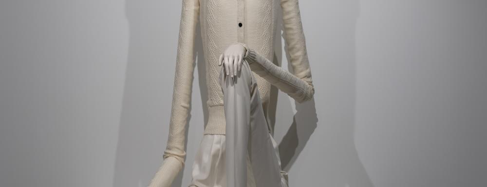 Human sculpture with white skin, white clothes and hair, extremely long limbs and torso
