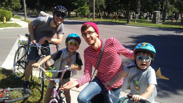 Group of people posing with bikes and helmets on as past Alley Cat participants.