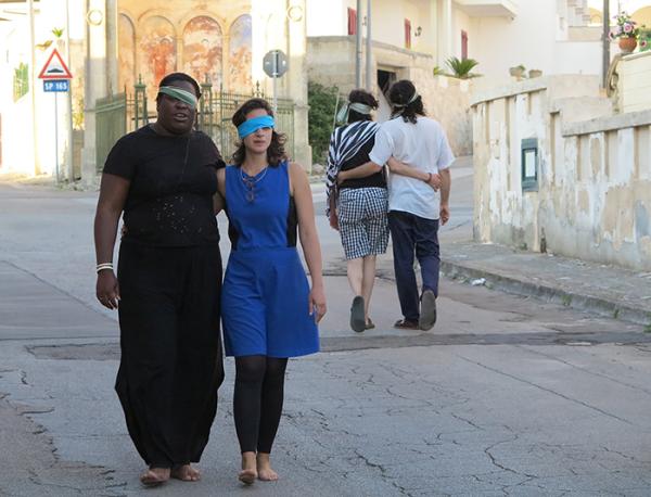 Two individuals walking down a street with each having one eye covered by a blind fold