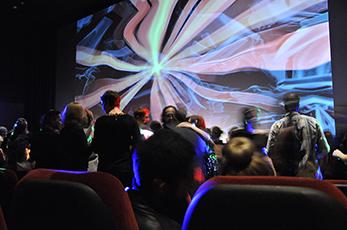 image of people gathering in theatre as abstract lines and colours are projected