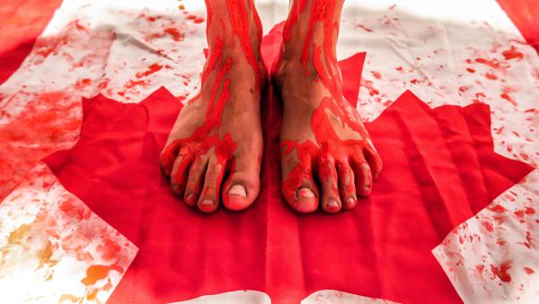 Photo of feet standing on Canadian flag with red paint splattered and dripping