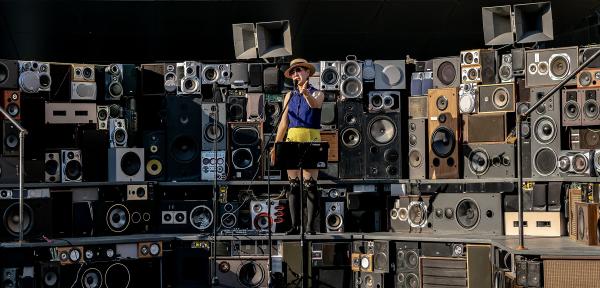 A performer is singing in the middle of a stage made of many stacked speakers